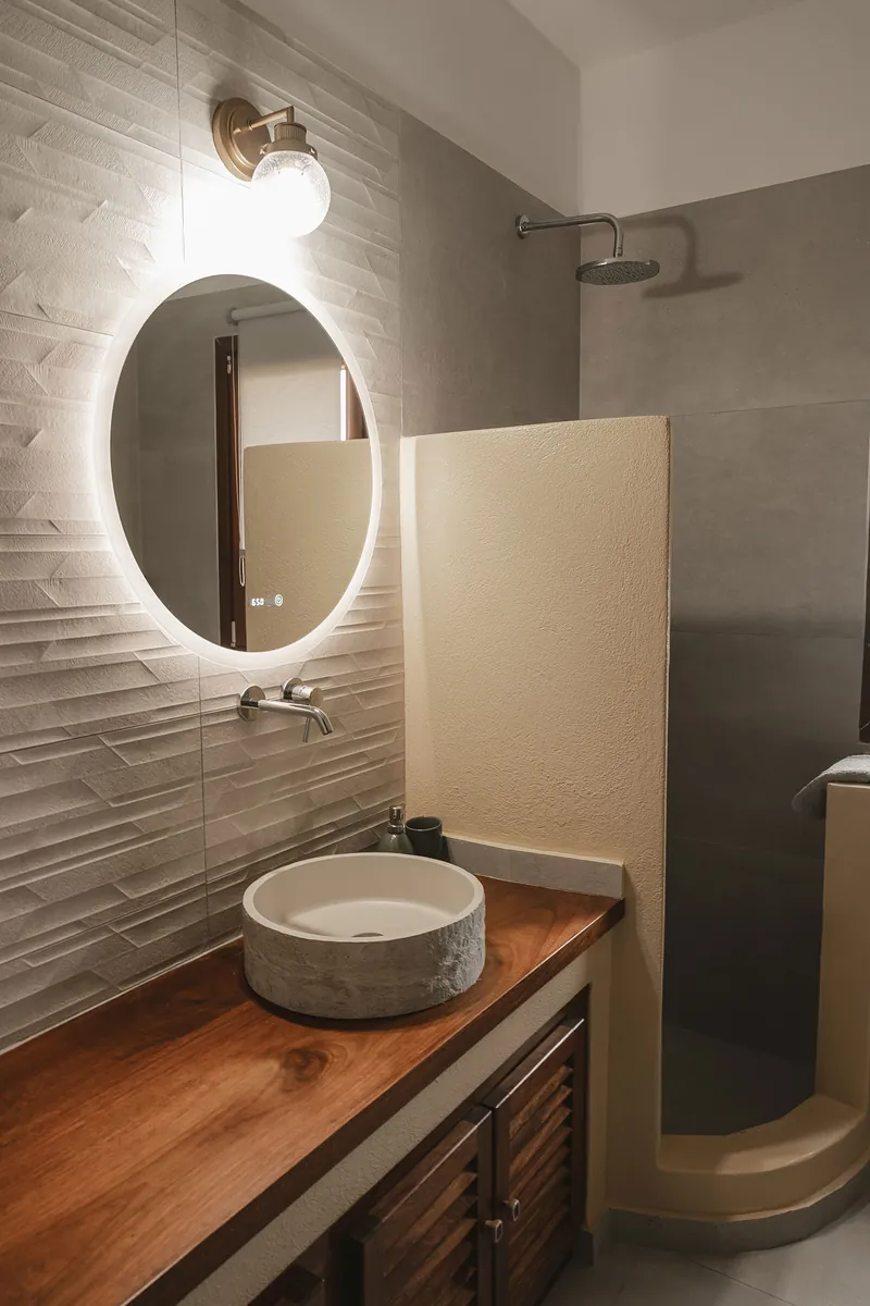 A bathroom with a round lit mirror and a stone basin