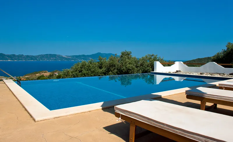 The infinity pool and loungers, with the sea and the mountains beyond