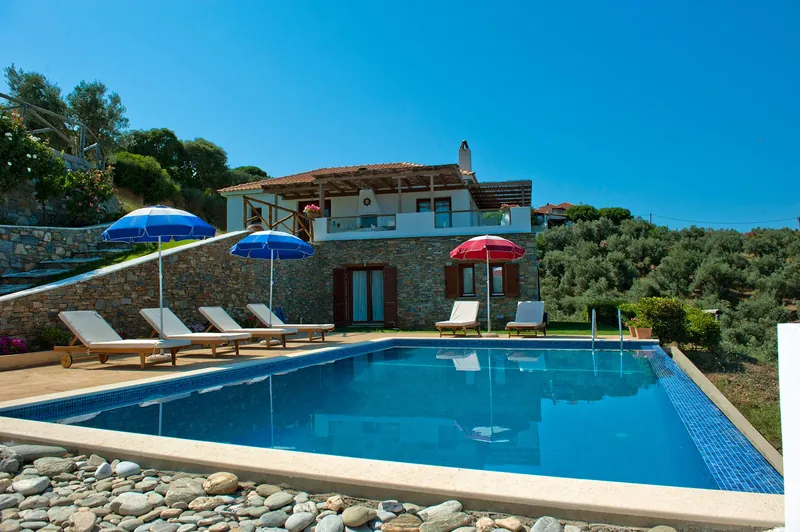 The stone villa behind its pool, under a blue sky